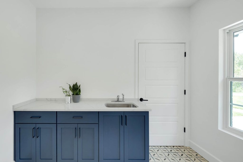 Modern kitchen with blue cabinets, white countertop, small sink, patterned tile floor, and a potted plant for freshness