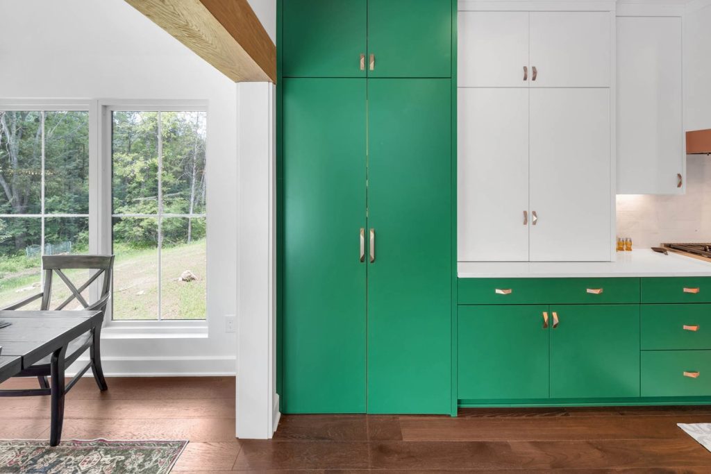 Kitchen with vibrant green lower cabinets, white uppers, silver handles, and a large window overlooking a lush garden.