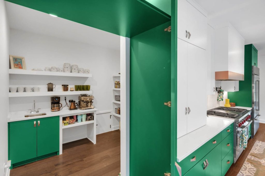 Kitchen with green cabinets, white countertops, open pantry shelves, and warm wood floors in a stylish, organized space.