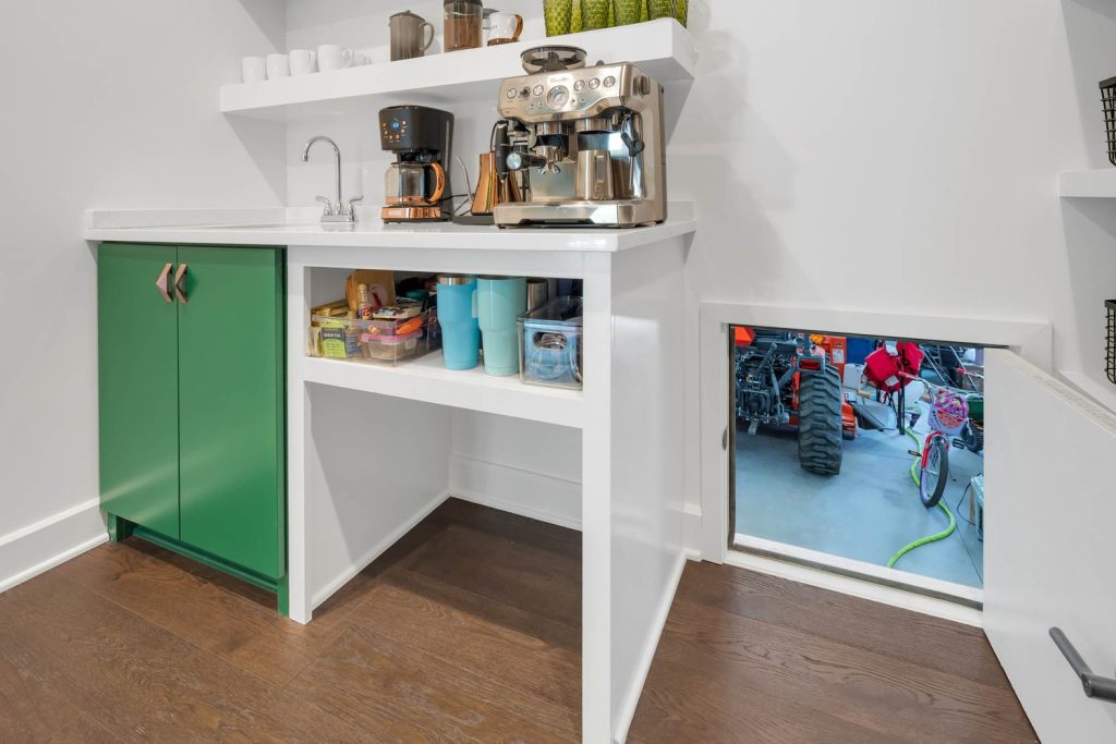 Kitchenette with coffee machine, mugs, snack shelf, and small door leading to a garage, combining cozy and functional design.