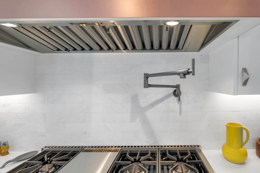 Kitchen with stainless steel pot filler, white tile backsplash, and sleek range hood in a calm, minimalist design.