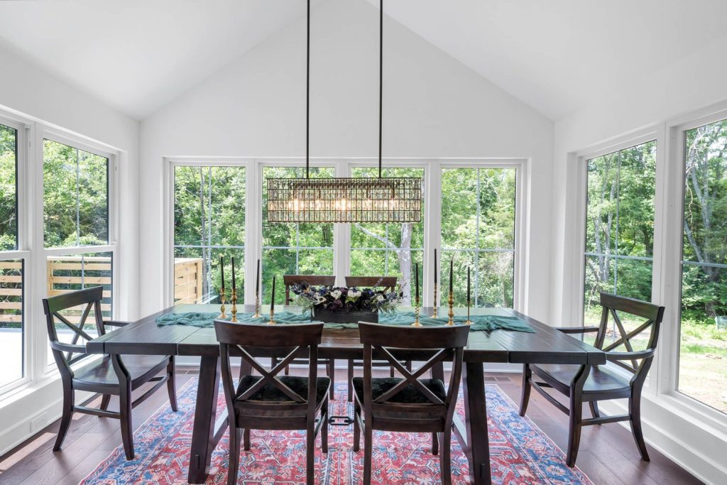 Dining room with dark wood table, black chairs, candle centerpiece, large windows, and modern chandelier overlooking greenery.