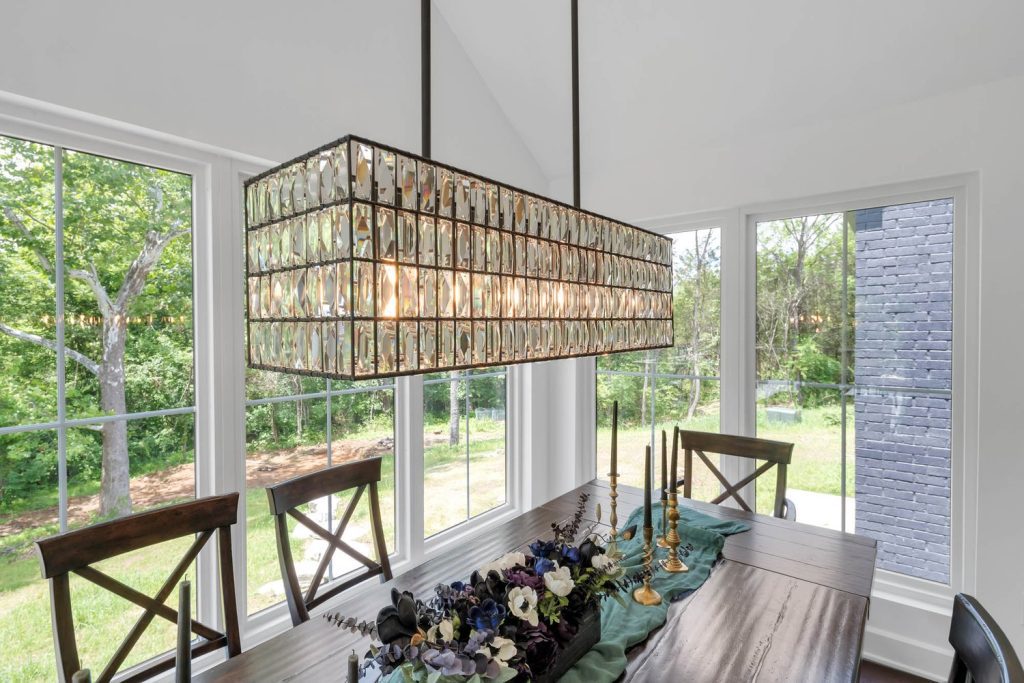 Rectangular crystal chandelier above wooden dining table with floral centerpiece and gold candlesticks, bright garden views.
