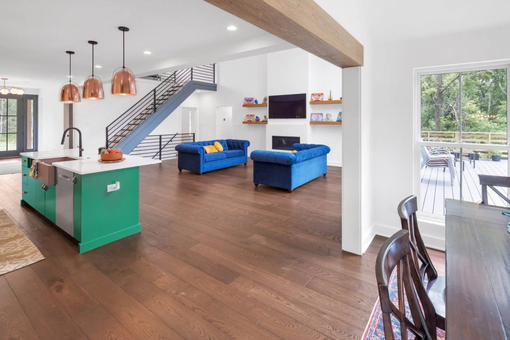 Living room with wooden floors, two blue sofas, fireplace with TV, colorful shelves, and copper pendant lighting.