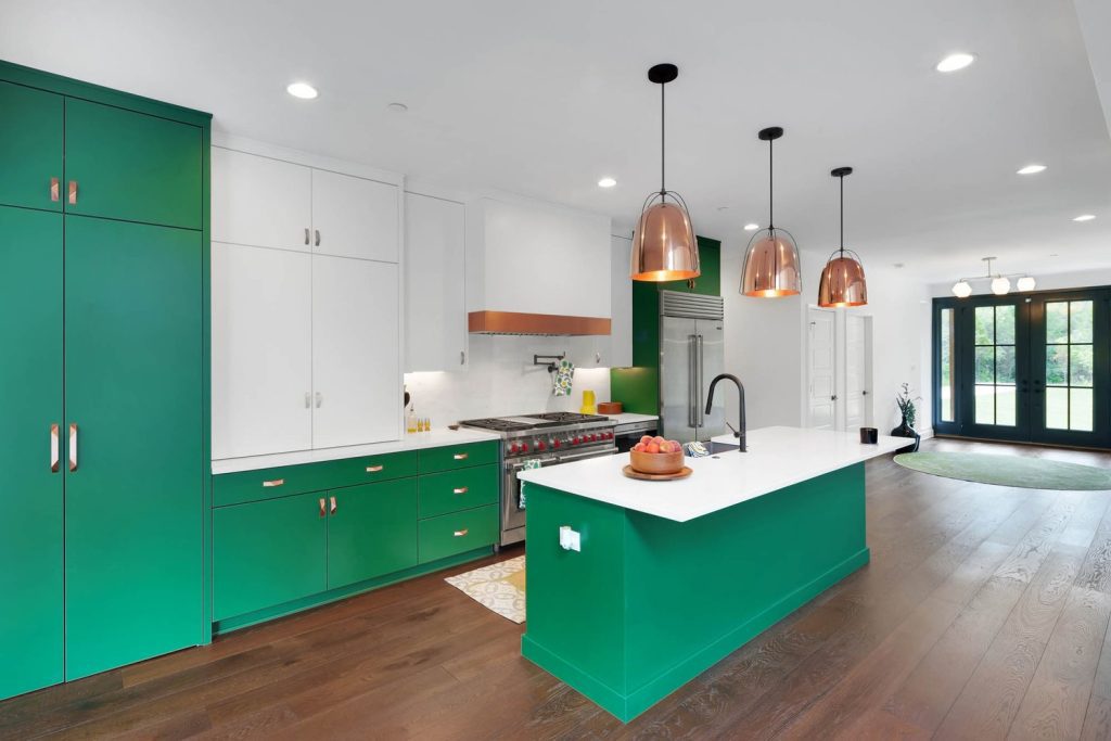 Kitchen with green cabinets, white island, metallic pendant lights, and a large window that fills the space with natural light.