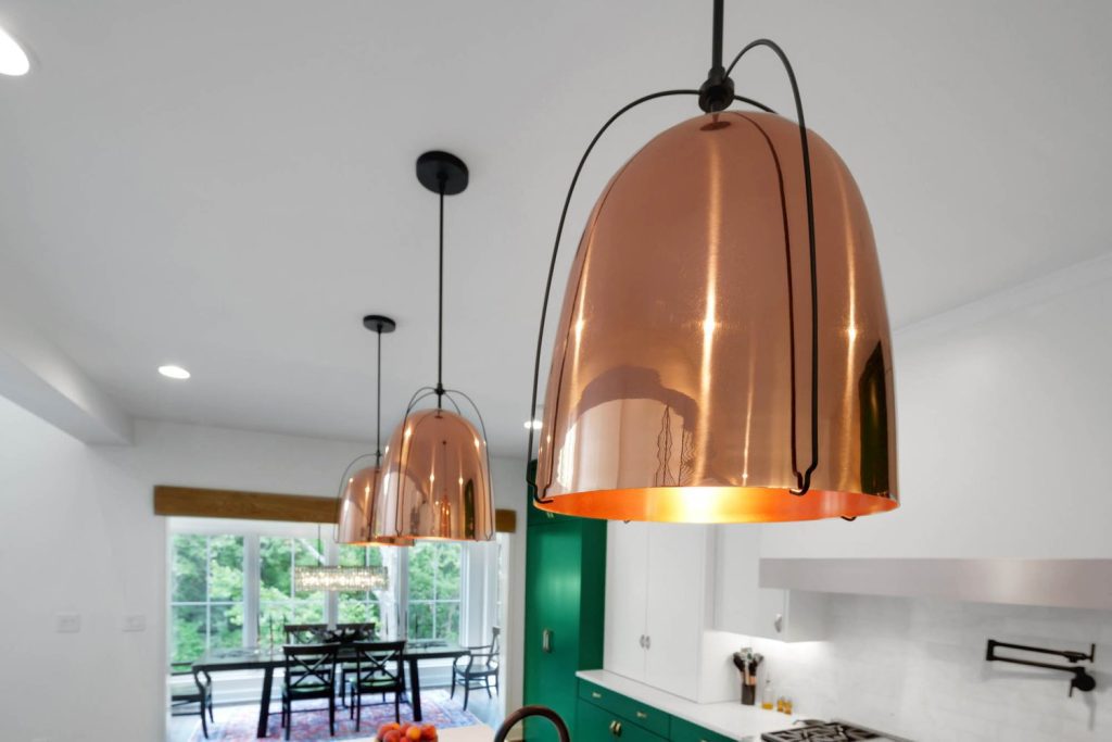 Modern kitchen with copper pendants, white cabinets, green accent wall, and dining area with bright windows