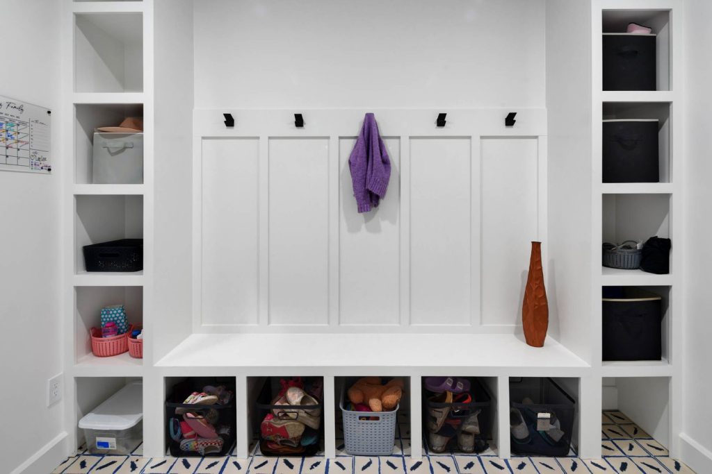 Mudroom bench with four cubbies, baskets and shoes, hooks holding a purple scarf, and a tall brown decorative vase