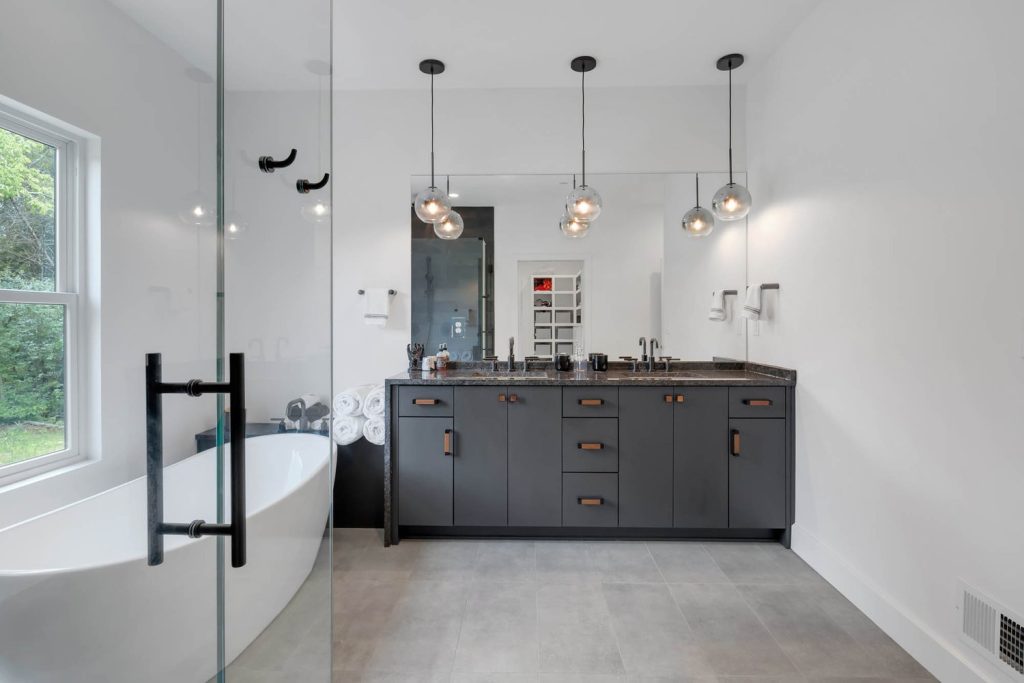Bathroom with black vanity, three globe lights, and white freestanding tub in a sleek, neutral-toned modern design