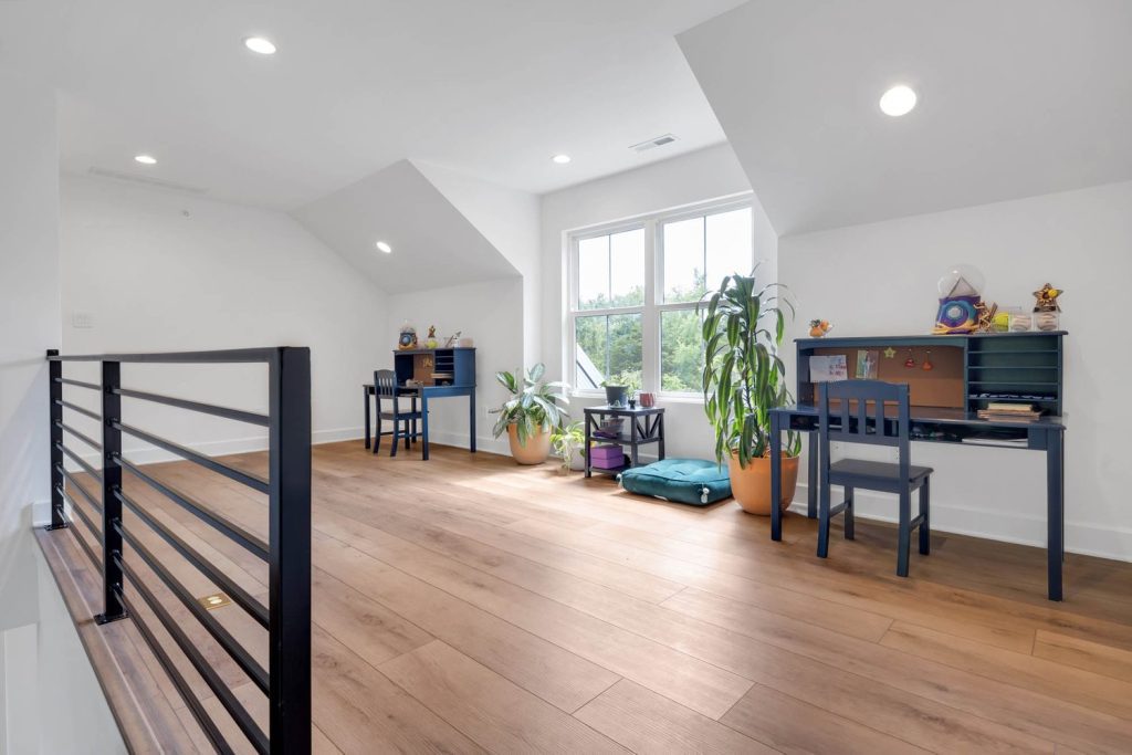 Bright attic home office with wood floors, two desks, large plants, and a big window creating a calm, airy workspace