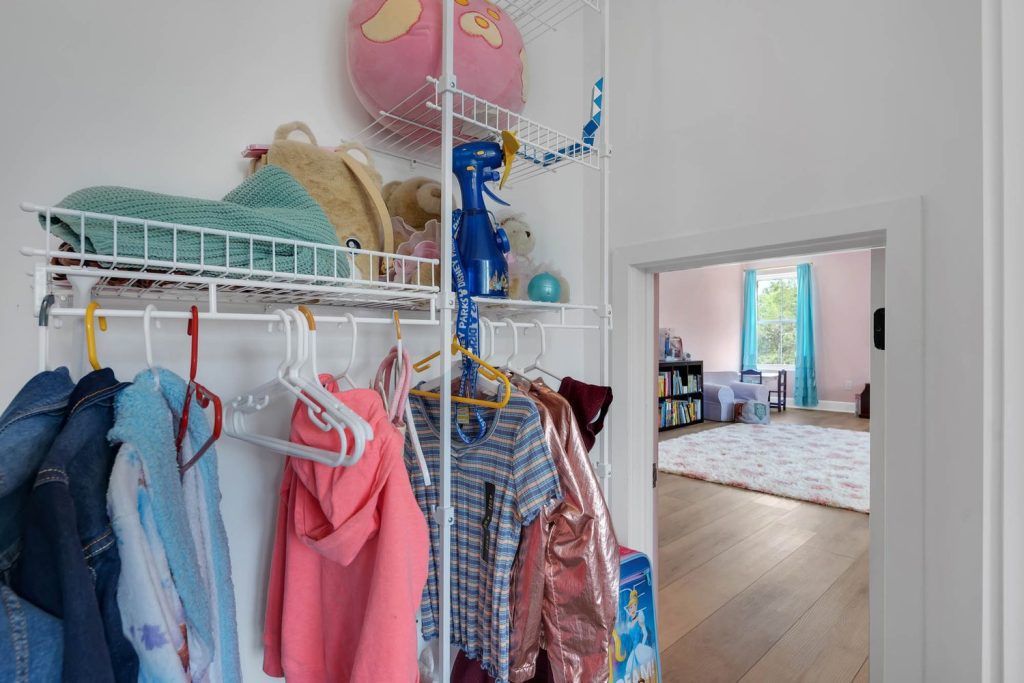 Child’s closet with colorful clothes and stuffed toys on shelves, opening to a bright playroom in a modern home