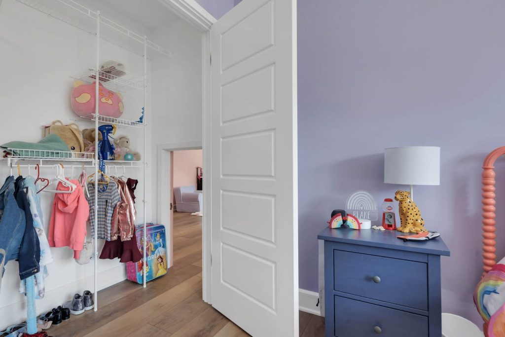Child’s bedroom with purple walls, blue dresser, and open closet showing toys and clothes in a cozy, playful modern home