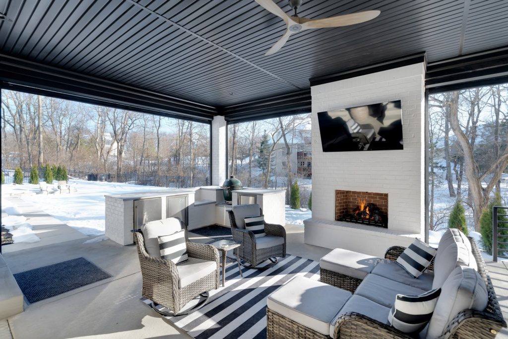 Covered patio in Louisville with wicker seating, striped cushions, and modern fireplace by top custom home builders.