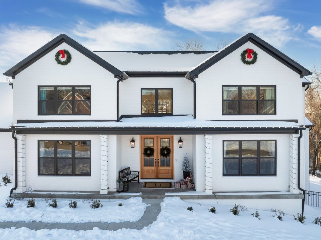 Two-story white custom home in winter by modern home builders with holiday wreaths and ribbons