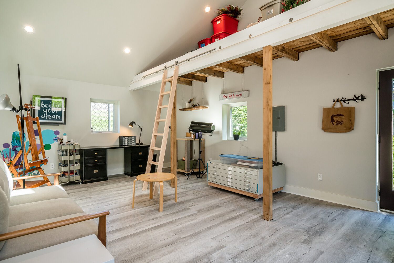 A bright, organized art studio with a vaulted ceiling, custom storage, and a wooden ladder, a unique space built by a custom home builder.