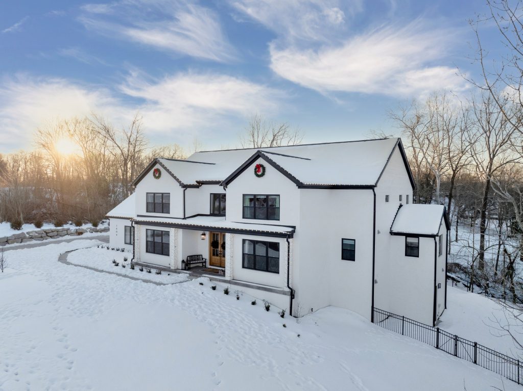 Snow-covered modern white house in Louisville with dark roof, designed by top custom home builders