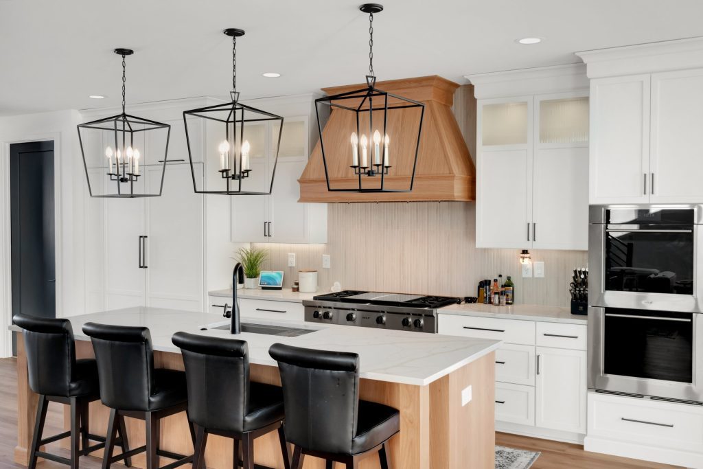 Stylish Louisville kitchen with white cabinets, wood range hood, black bar stools, and geometric pendant lights by top custom home builders.