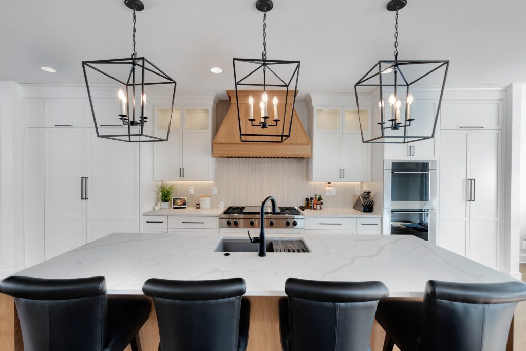 A modern kitchen with a marble island, white cabinets, and a wooden range hood, a beautiful example of custom home design by Eldridge Company.