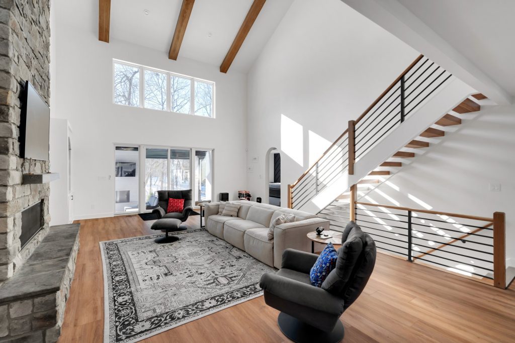 A modern living room with a high ceiling, wooden beams, and a stone fireplace, part of a luxury custom home built by Eldridge Company.