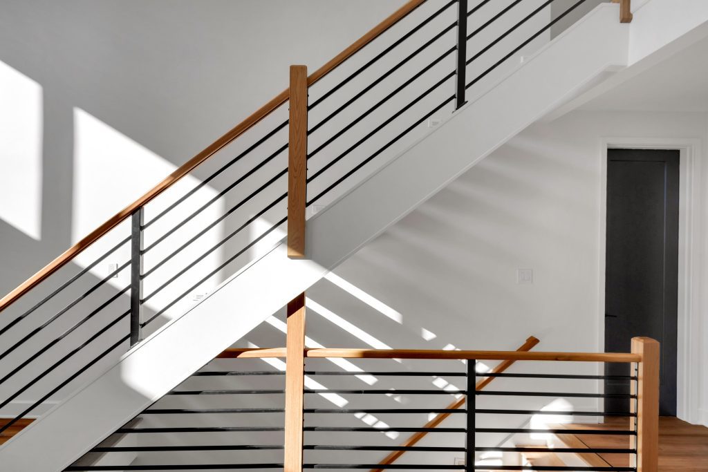 A modern and minimalist staircase with wooden handrails and black balusters, a stunning design element in a new custom home by Eldridge Company.