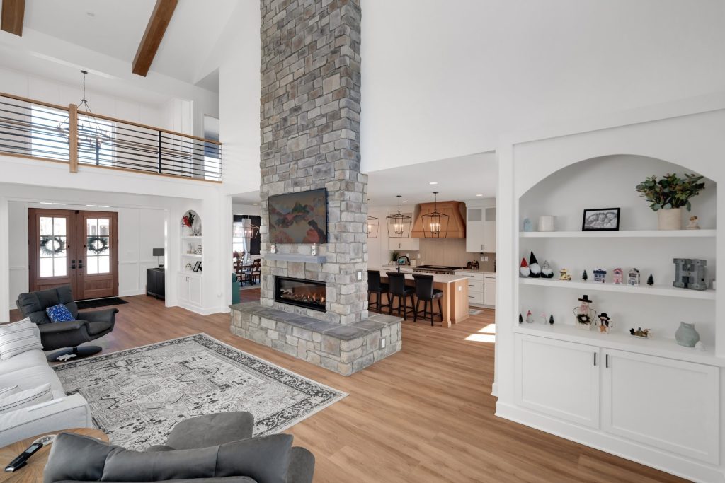 A spacious living area with a stone fireplace, wooden beams, and a modern kitchen, showcasing a cozy custom home built by Eldridge Company.
