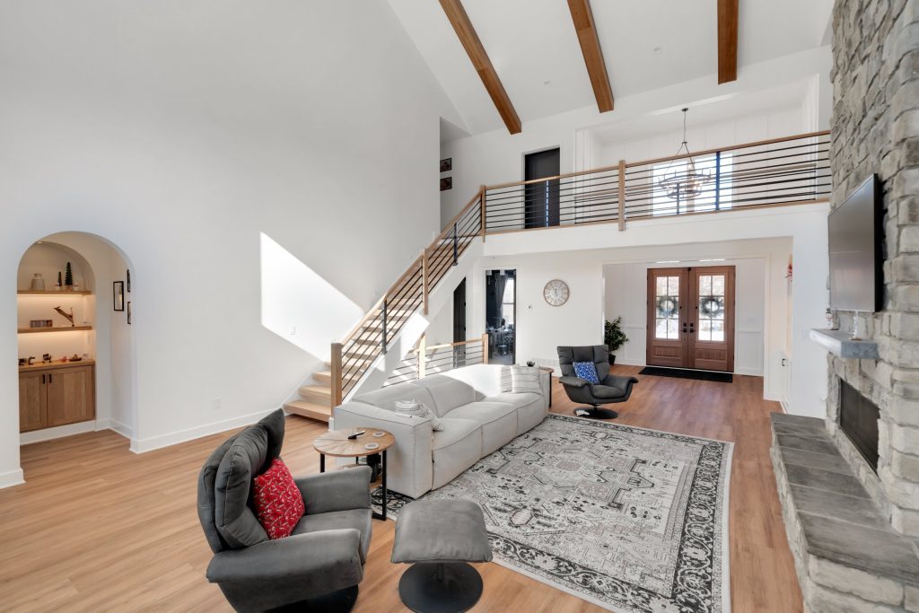 A spacious living room with high ceilings, wooden beams, and a stone fireplace, part of a beautiful custom home by Eldridge Company.