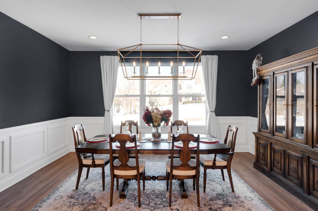 Sophisticated dining room with dark walls, a wooden table set for four, elegant chairs, a floral centerpiece, and large windows with white curtains.