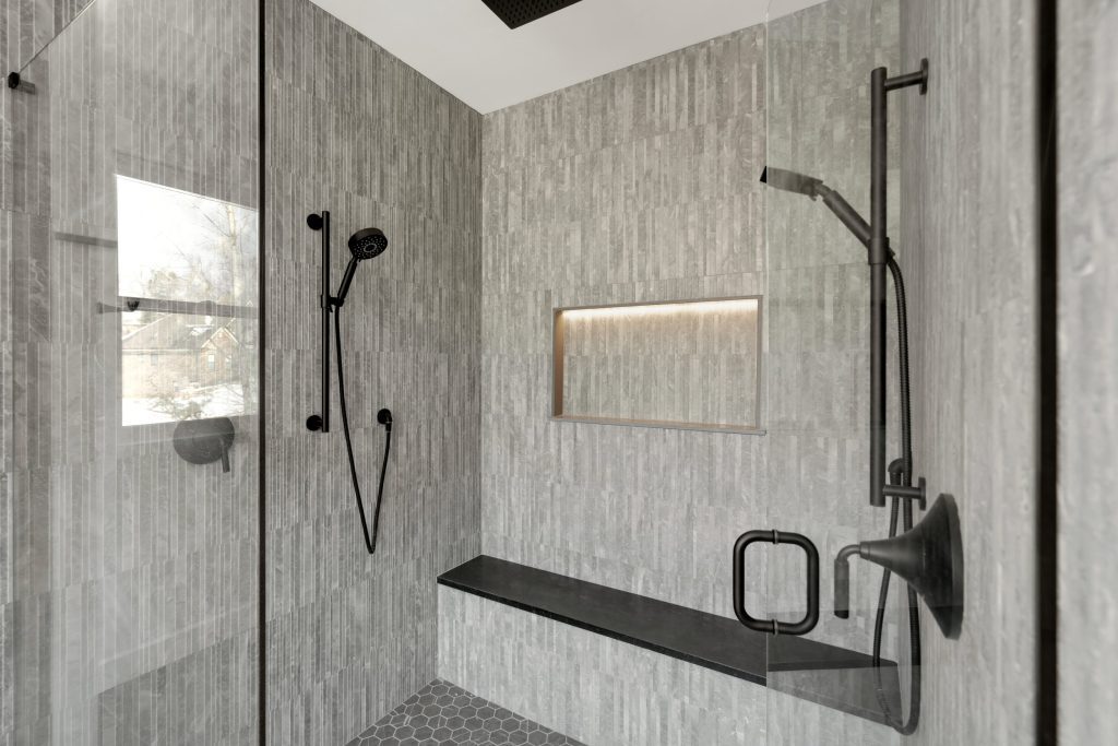 A modern, custom walk-in shower with sleek gray tiles, a matte black shower system, and a built-in bench, all part of a luxurious custom home.