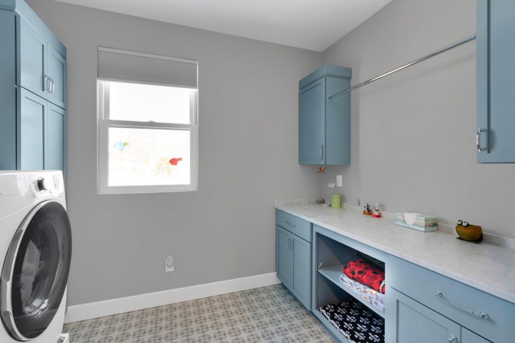 Custom home design in Louisville, KY showing laundry room with bright window, washer, and blue cabinets.