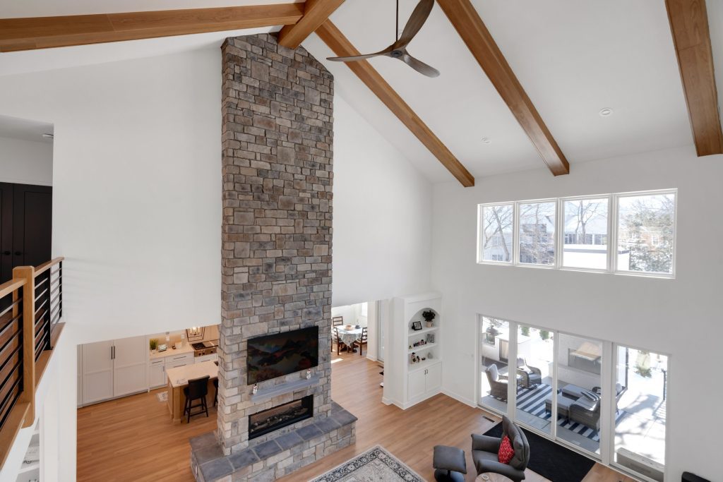 Louisville luxury custom home living room with bright windows, wooden beams, and stone fireplace.