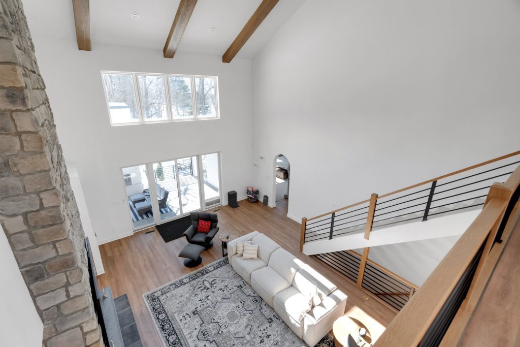 Spacious contemporary living room in custom home with patterned rug, stone fireplace, and large windows.