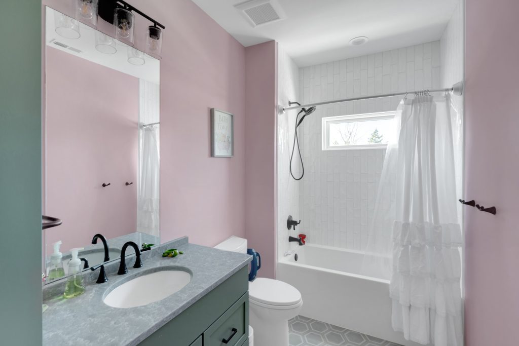 Louisville modern bathroom with pink walls, gray countertop, white tub, and black fixtures for a stylish look.