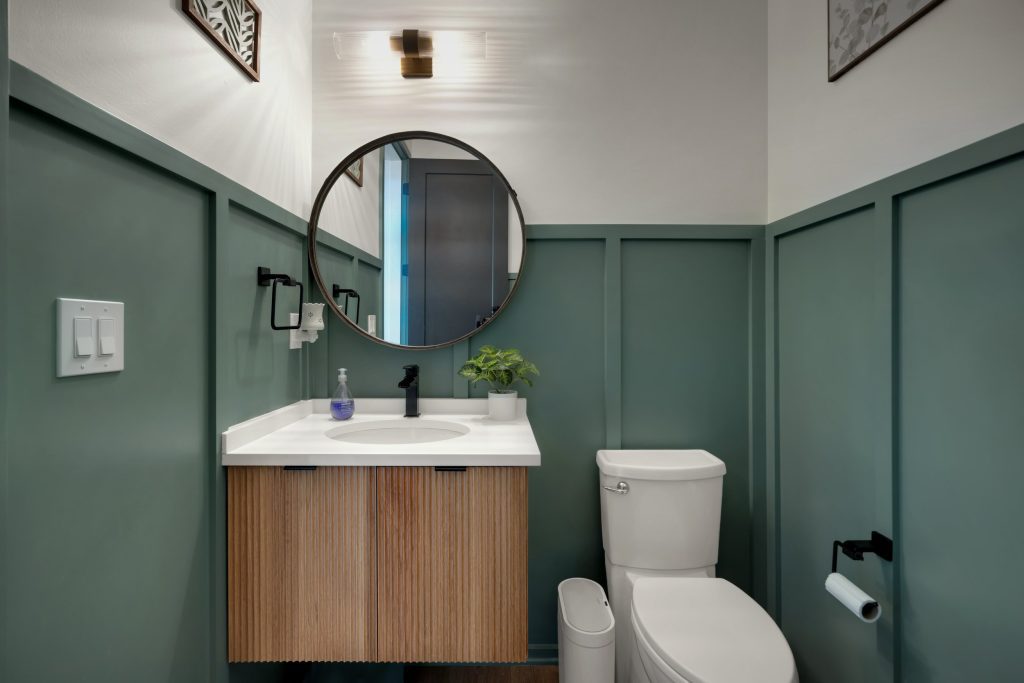 Louisville modern farmhouse bathroom with green paneling, wooden vanity, round mirror, and minimalist warm design.