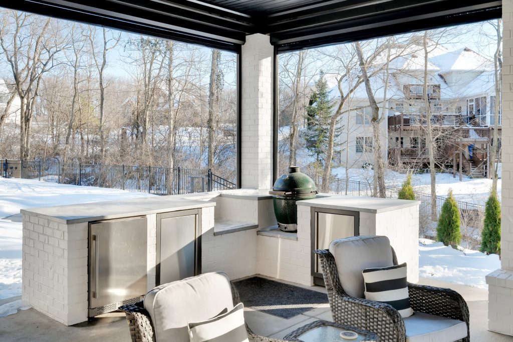 Louisville modern outdoor lounge by top custom home builders featuring wicker seating, table, and snowy view through large windows.