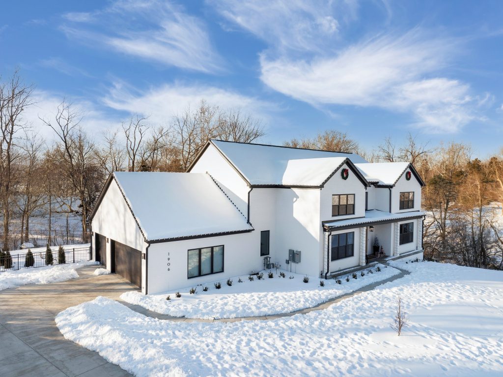 Snowy Louisville home with sleek white exterior, dark roof, and winter landscaping by top modern home builders Eldridge Company.