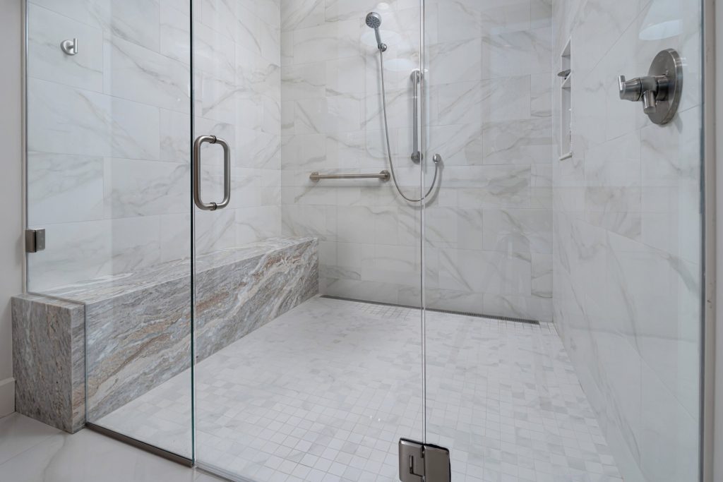 Louisville modern bathroom shower with marble walls, glass door, and built-in bench by top custom home builders.