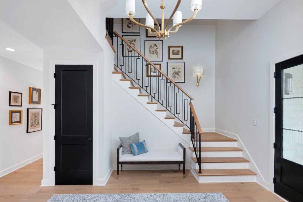Louisville modern entryway with wooden staircase, black railings, and chandelier by top custom home builders.