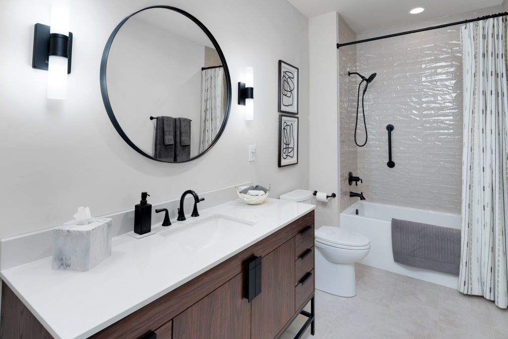 Louisville modern bathroom with round mirror, white vanity, black fixtures, and sleek design by top custom home builders.