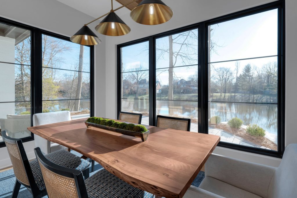 Louisville modern dining room with wooden table, wicker chairs, and lake view by top custom home builders.