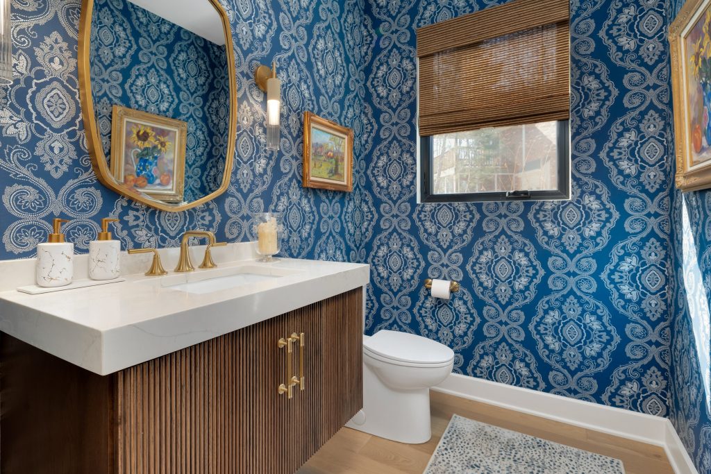 Luxury modern bathroom with blue and white wallpaper, gold fixtures, and custom vanity by top modern home builders.