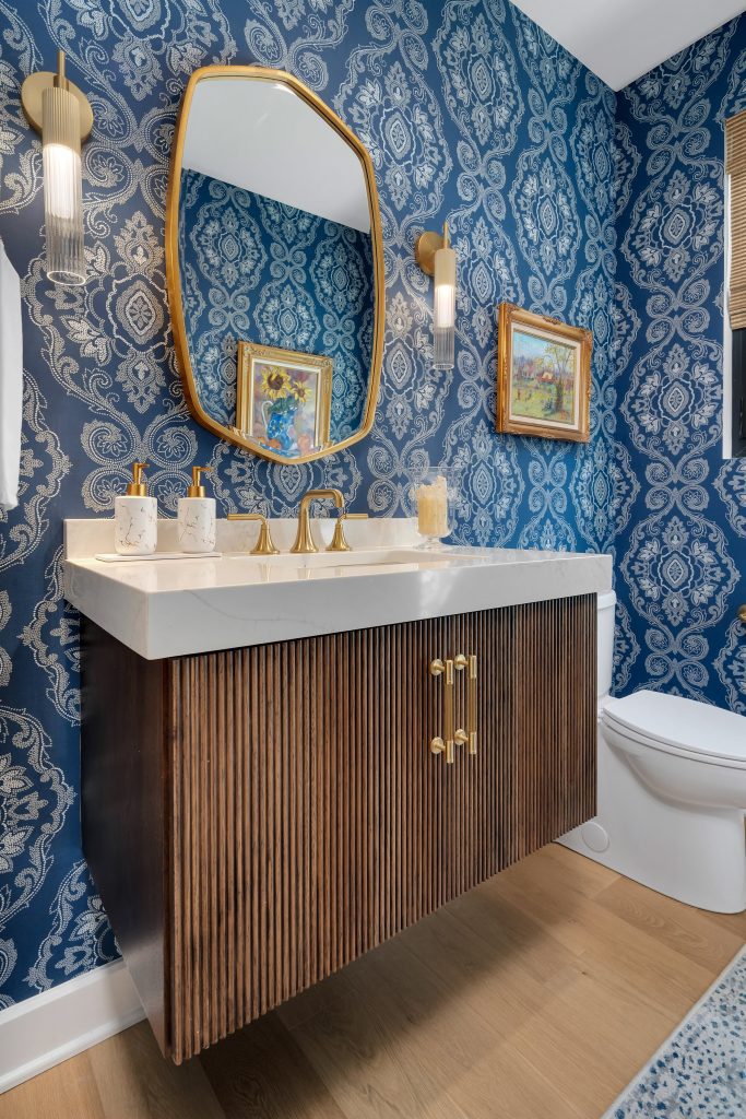 Elegant modern bathroom with blue and white damask wallpaper, gold fixtures, and custom wood vanity by top modern home builders.