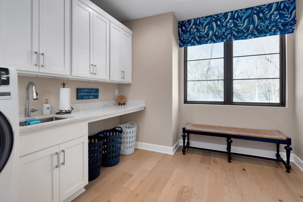 Bright modern laundry room with white cabinetry, light wood floors, and custom storage by top modern home builders.