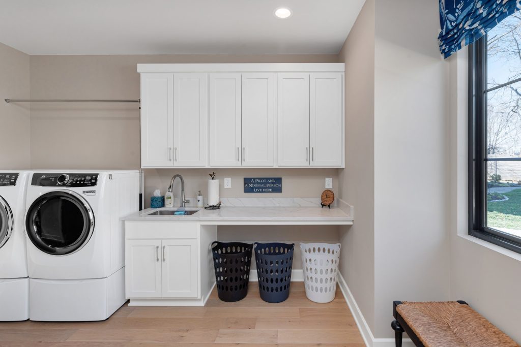 Modern Louisville laundry room with white cabinets, washer, and baskets by top custom home builders
