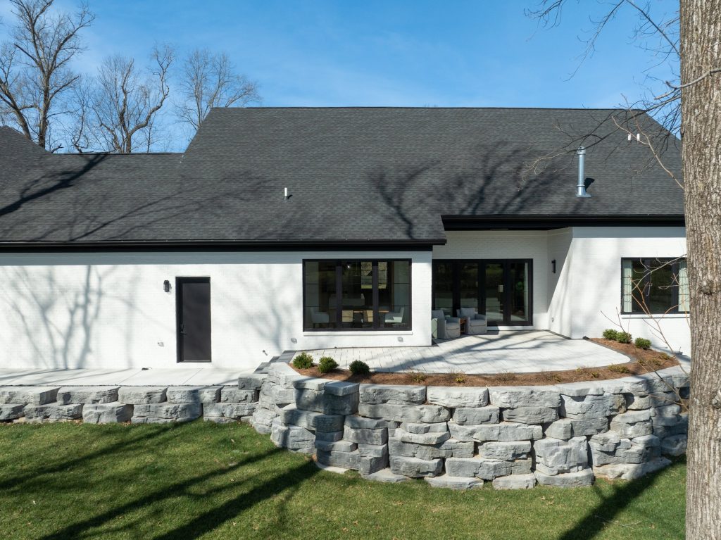 Modern Louisville white home by a pond with dark roof and green lawn, designed by top custom home builders
