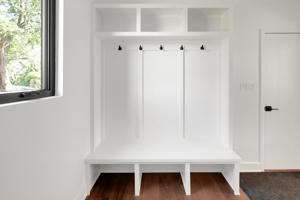 Modern Louisville mudroom design featuring white bench, cubbies, hooks, and natural light.