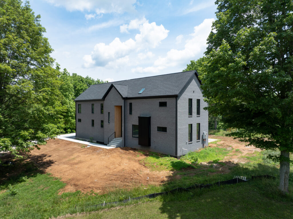 Luxury Louisville home with dark gray brick exterior, central entrance, and lush surroundings.