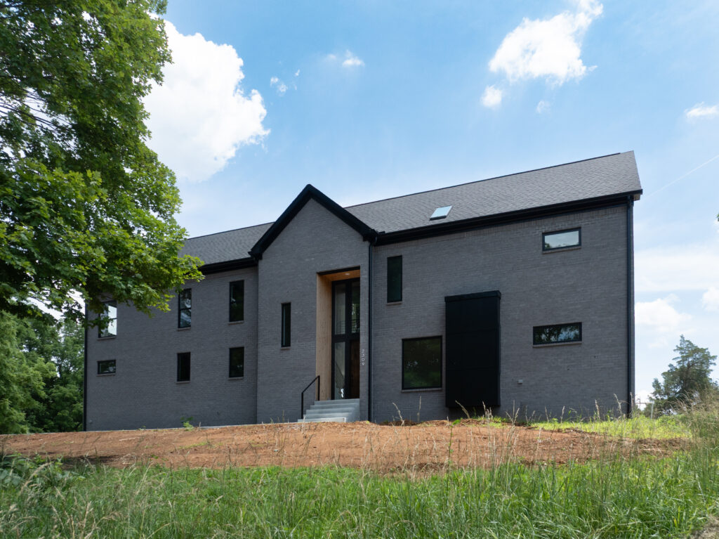Luxury Louisville home with dark gray brick exterior, central entrance, and lush surroundings.