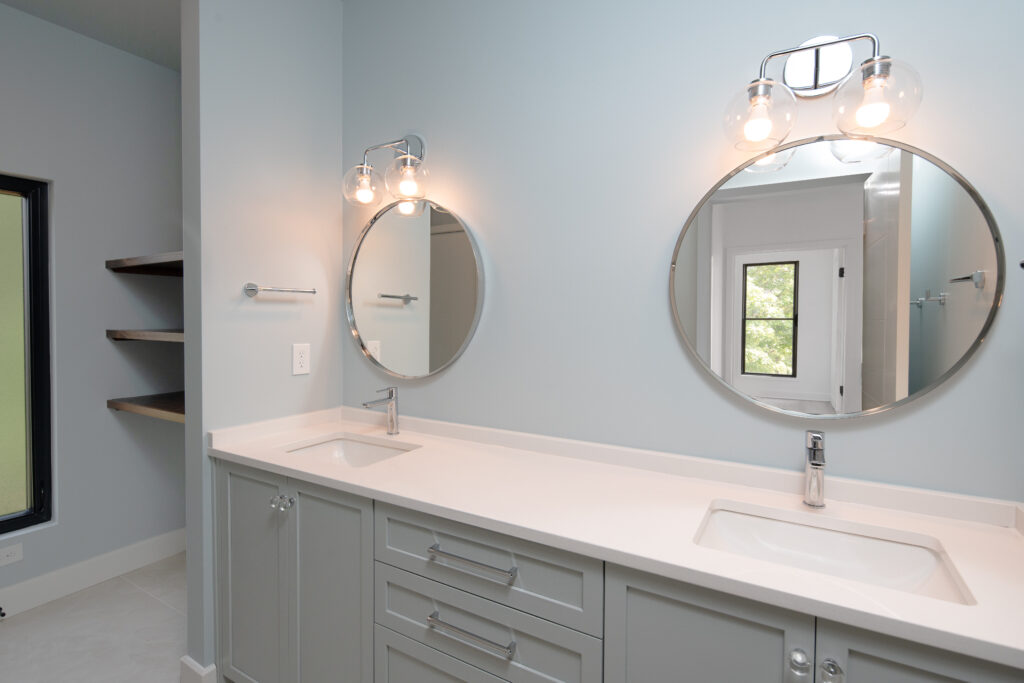 Louisville luxury custom home bathroom with light blue walls, double vanity, round mirrors, and window accents.