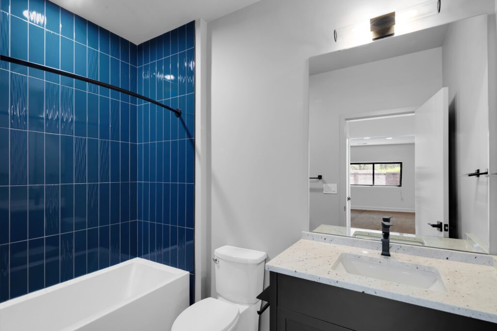 Modern bathroom in Louisville home with white tub, deep blue tiles, and large mirror.