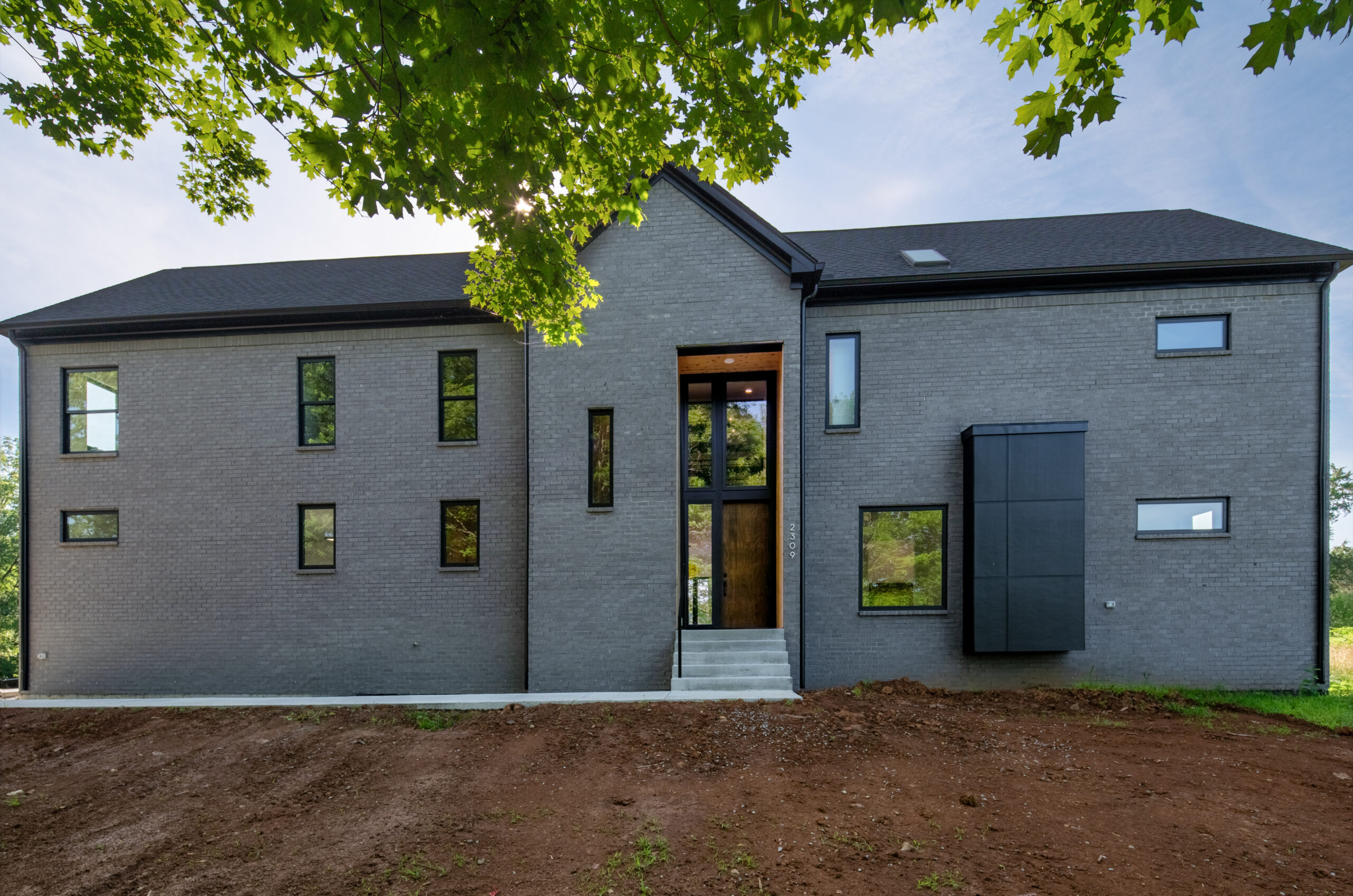Modern Louisville home design with gray brick, black-framed entry, and green leaves framing.