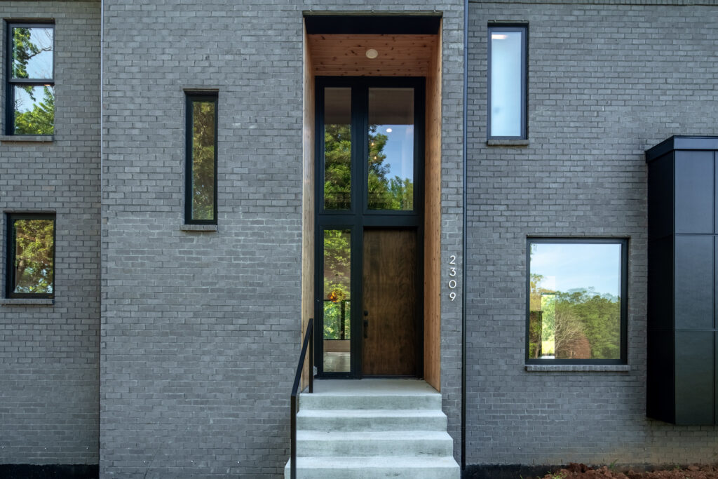 Custom Louisville home with two-story modern design, concrete patio, and large windows. Luxury Louisville home exterior with gray brick, sleek entry steps, and tall windows.